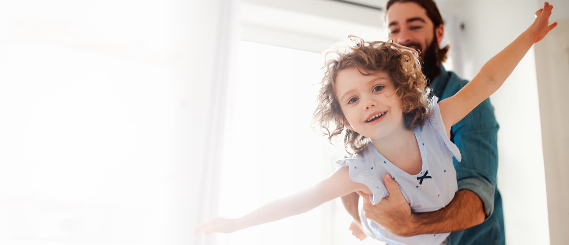 Ein Vater hält ein junges Mädchen in den Armen, das Flugzeug spielt.
